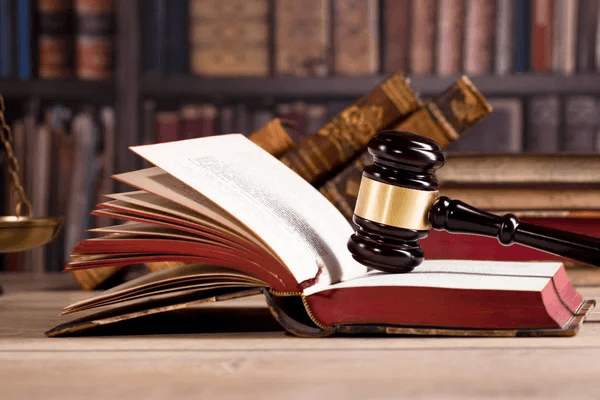 Libro jurídico abierto con mazo de madera sobre las páginas, fondo de biblioteca; imagen simbólica de derecho y derechos humanos.