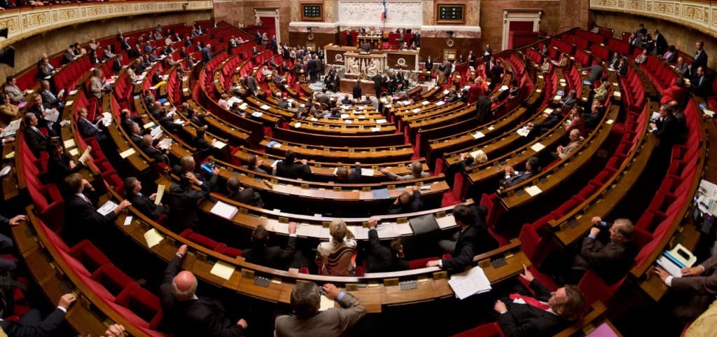 Hemiciclo de la Asamblea Nacional francesa (Palais Bourbon, París) durante una sesión parlamentaria, con escaños rojos en semicírculo y estrado central.