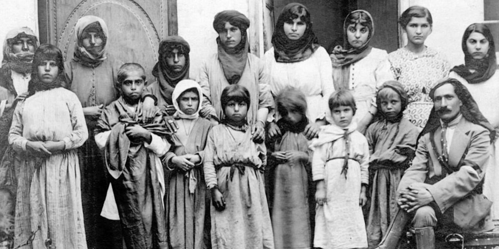 Retrato de grupo en blanco y negro: varias mujeres, niños y un hombre sentado frente a muro claro.