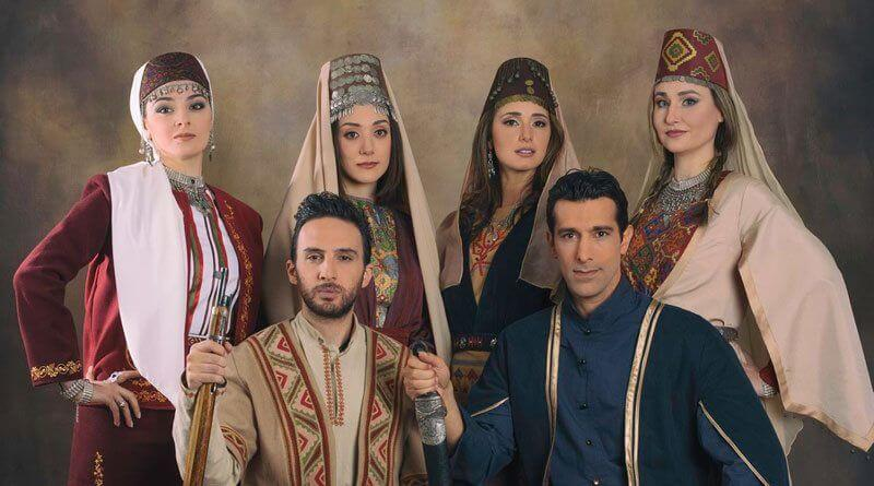 Retrato de estudio de seis personas con traje popular armenio regional — taraz bordado, tocados y platería; dos hombres sentados con fusil y espada.