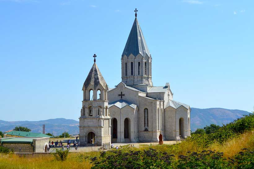 Catedral Ghazanchetsots del Salvador Santo y campanario gemelo en piedra caliza clara, techos cónicos y cruces, montañas al horizonte.