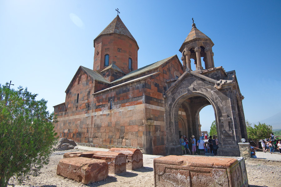 Monasterio de Khor Virap con cúpula cónica, relieve tipo khachkar en el pórtico, tumbas antiguas en el patio, visitantes junto a la puerta.
