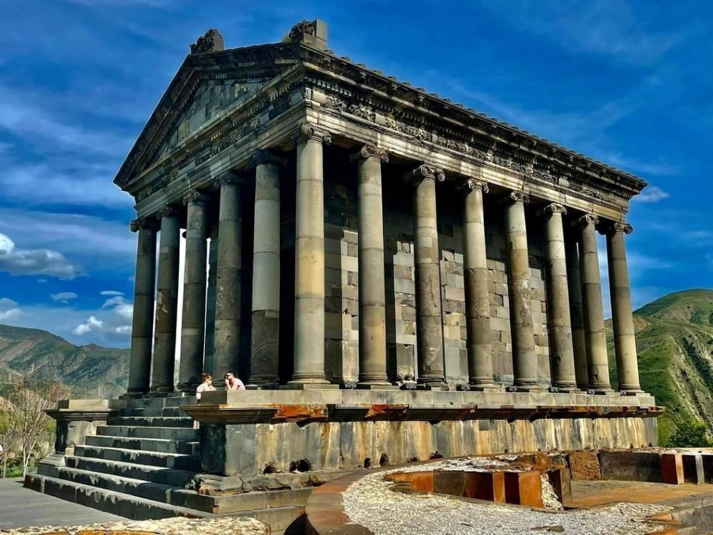 Templo de Garni, santuario períptero de basalto con columnas jónicas y podio escalonado, garganta verde y montañas al fondo.
