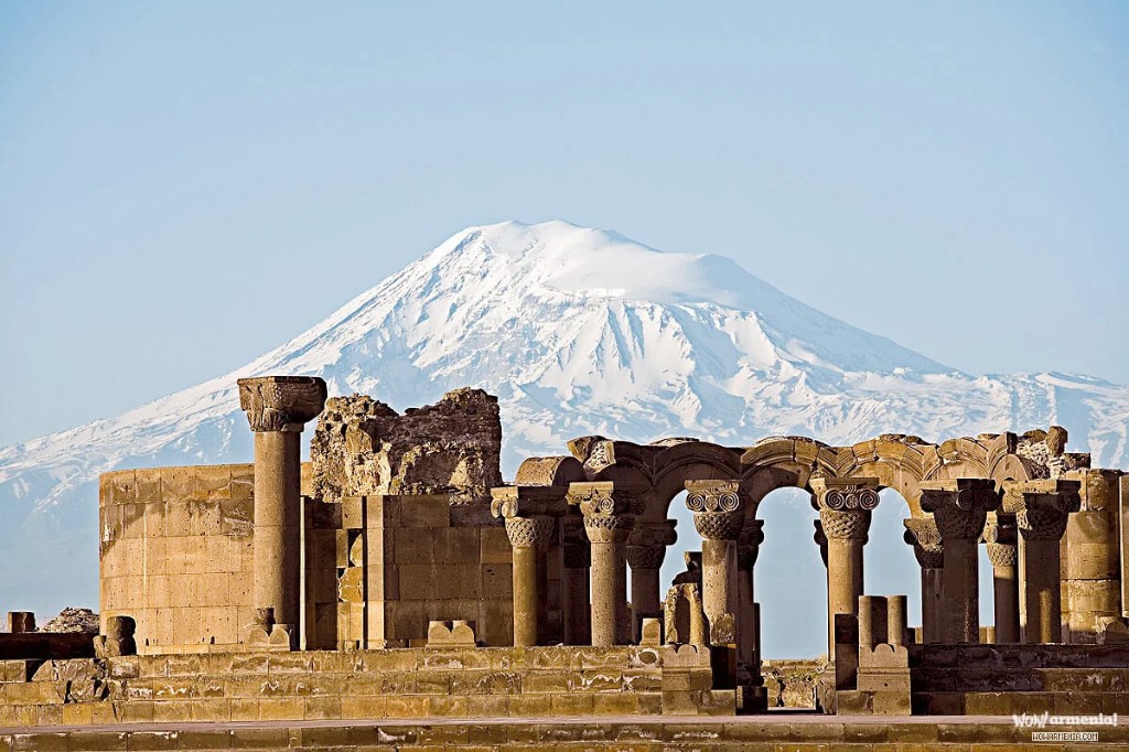 Ruinas de la catedral de Zvartnots: columnas altas con capiteles tallados y arcos, monte Ararat nevado al fondo.