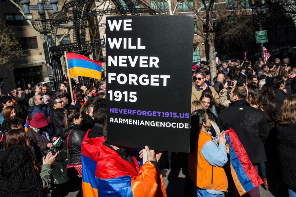 Conmemoración en la calle: persona con bandera de Armenia sostiene cartel We Will Never Forget 1915 y neverforget1915.us.